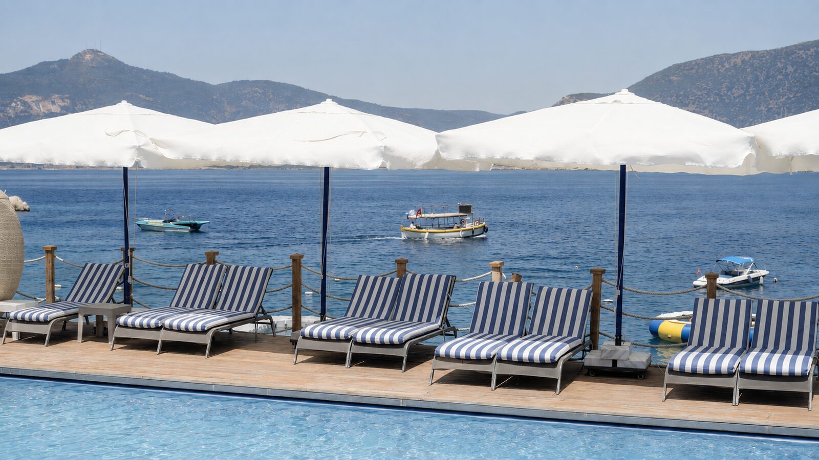 The pool terrace, sunbeds and boats in the bay
